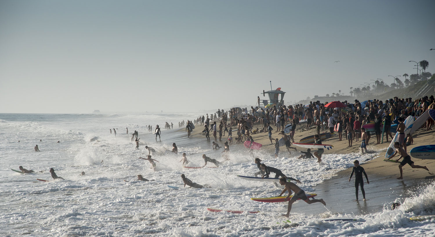 A mass of surfers crowd the beach and run into the water.