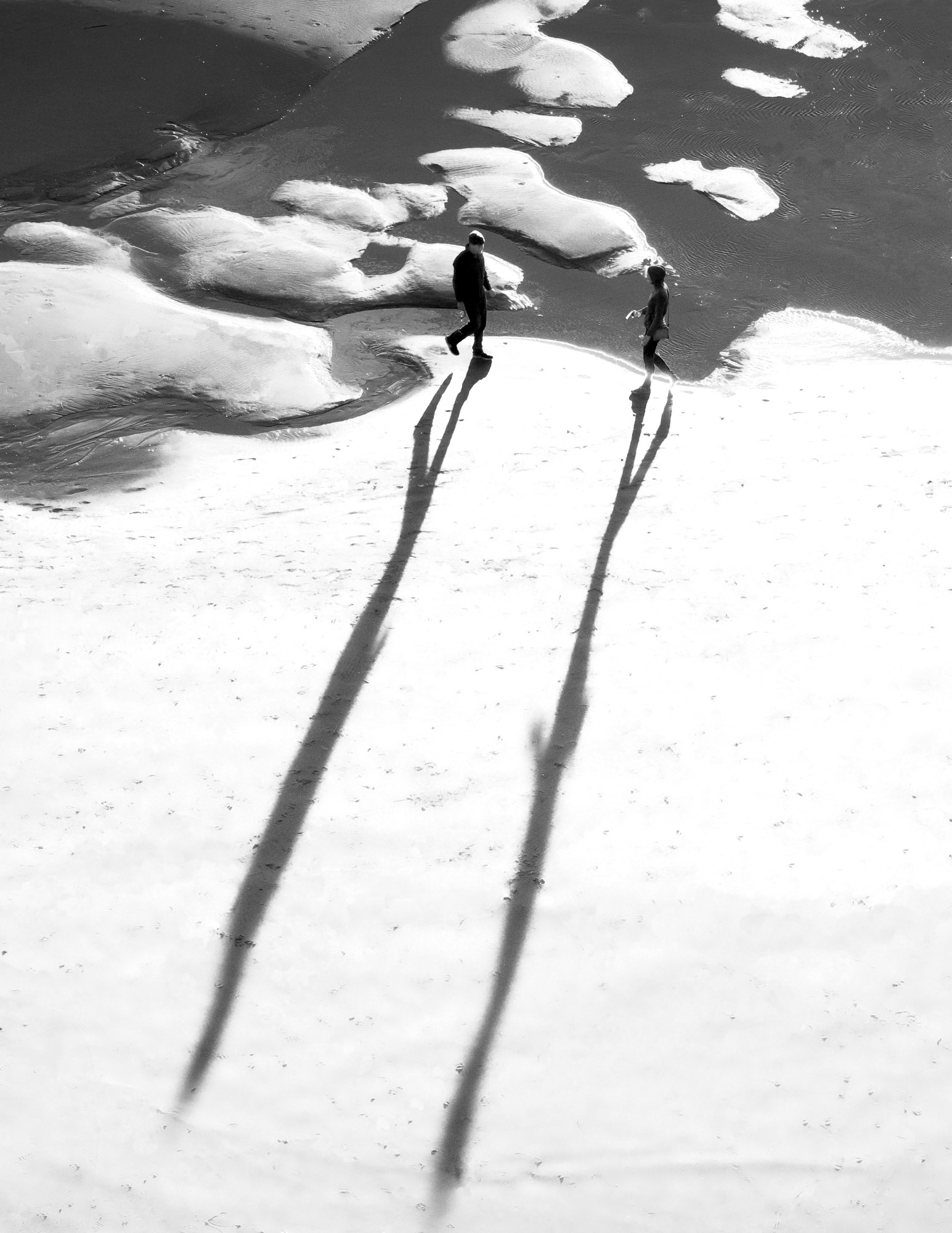 seen from above, two people walk on a beach, their shadows long
