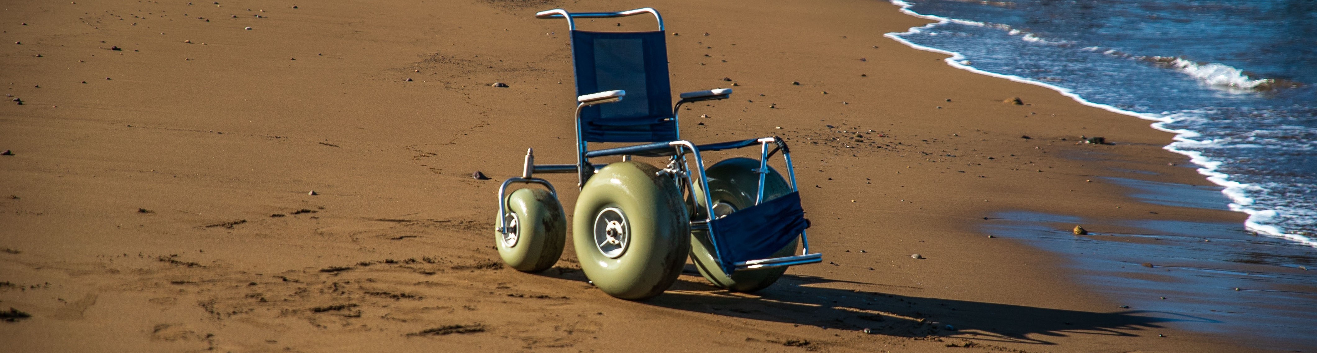 An unoccupied beach wheelchair sits on the sand