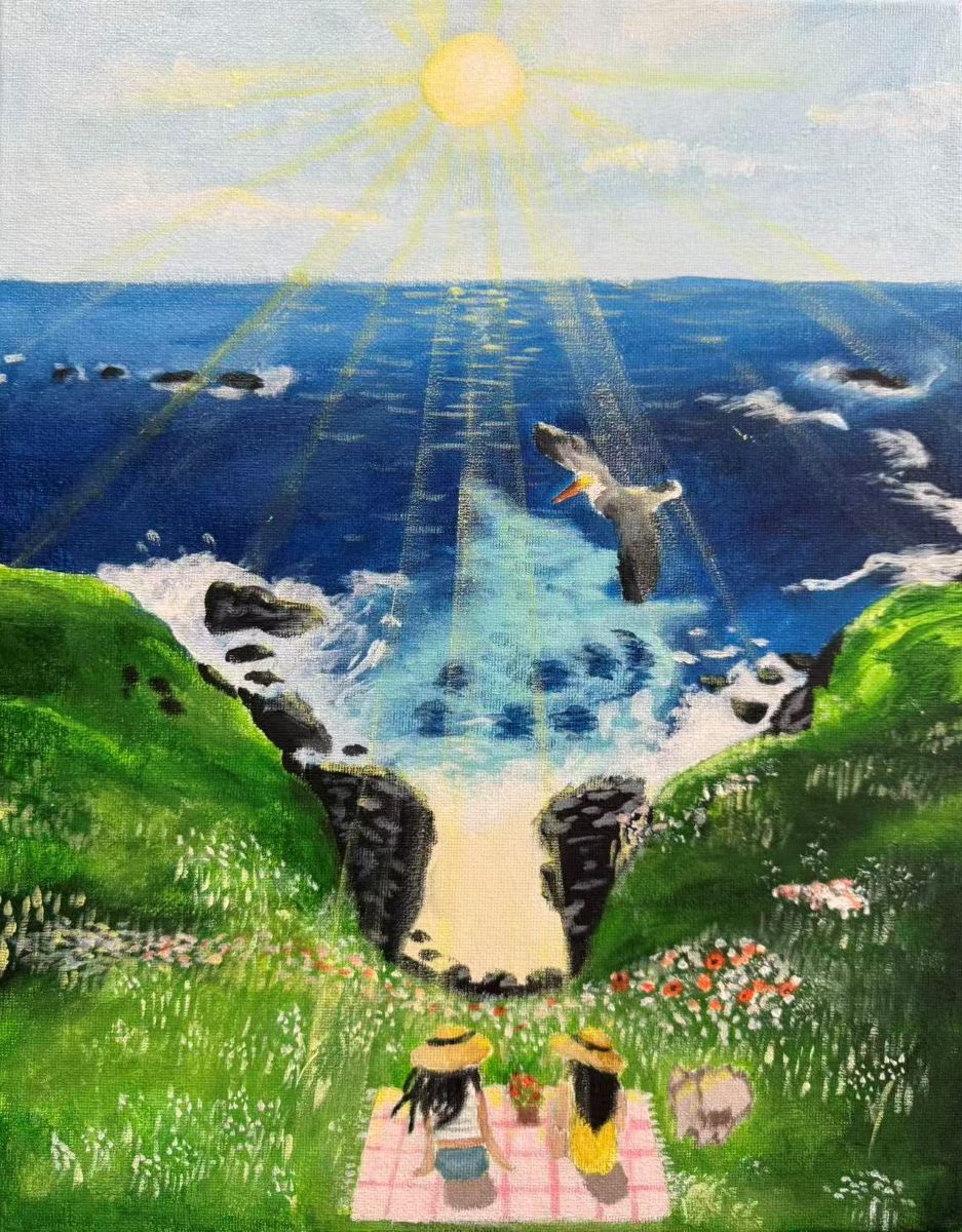 Two girls sit on a pink picnic blanket. They are sitting on a grassy cliff overlooking the ocean. The waves are crashing on the rocks and shore below. The sun is shining bright and a pelican is flying overhead.