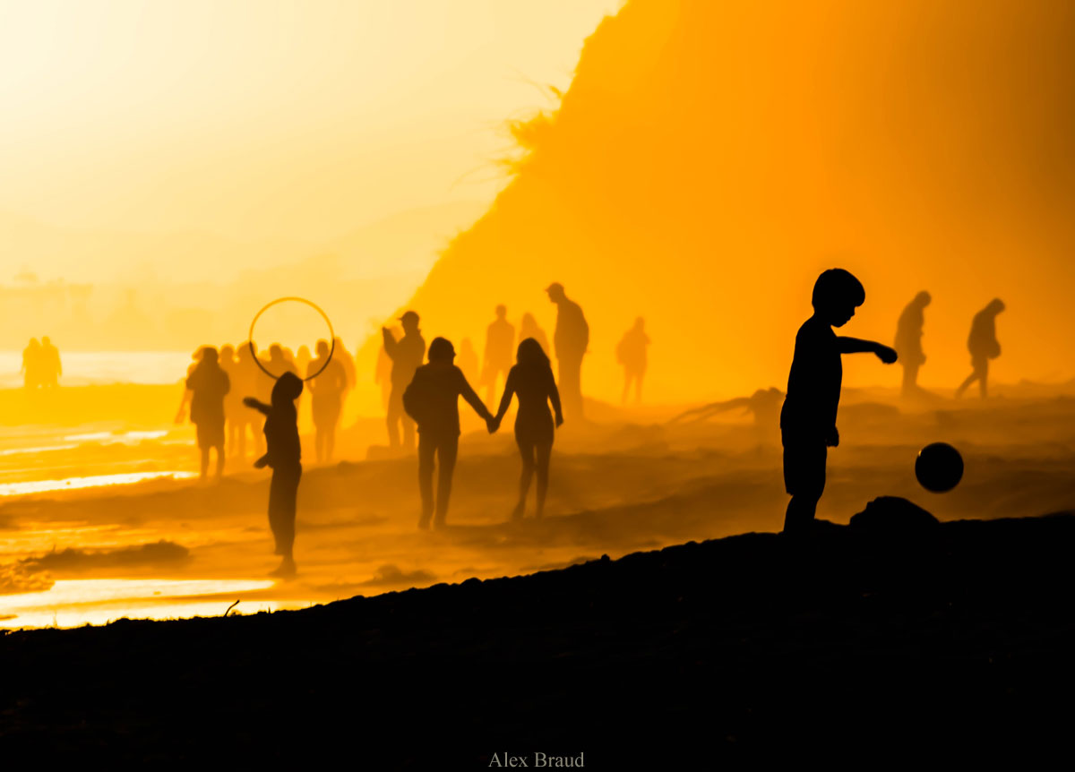 Photo of adults and children playing on Hendry's Beach, in silhouette in front of yellow sunset, by Alex Braud