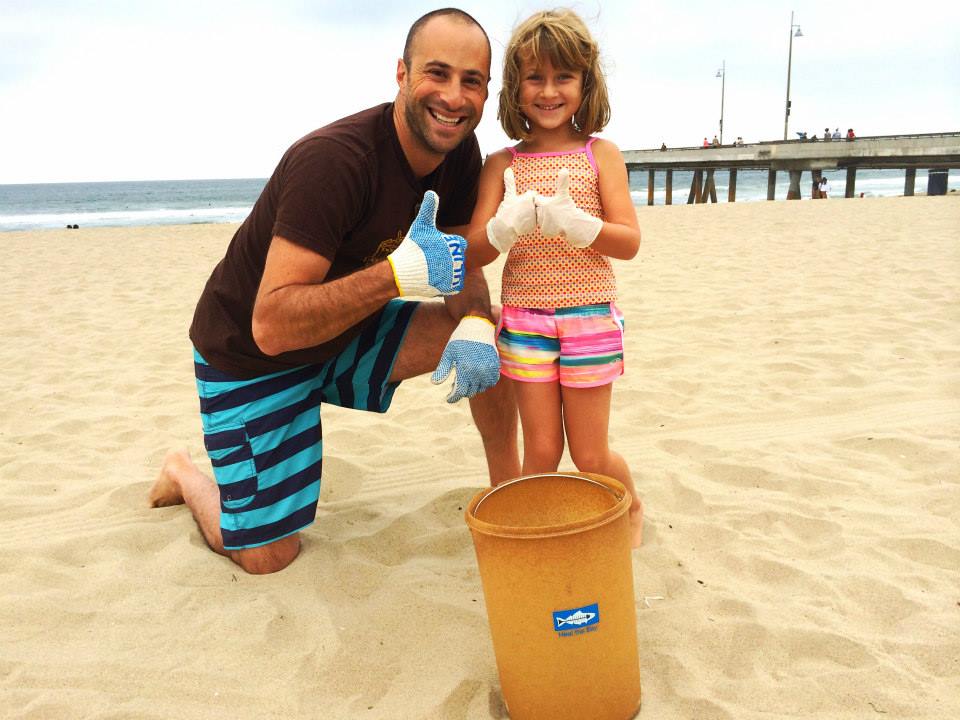 Dad and child on the beach with their trash bucket, giving thumbs up