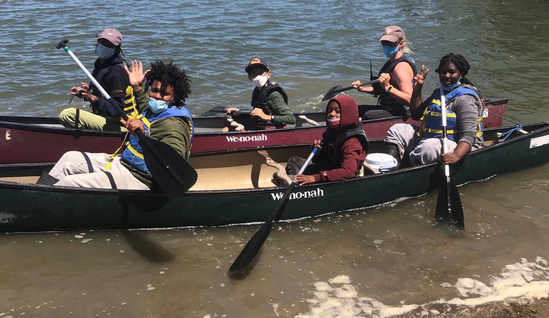 A group of youth and adults wave from a canoe