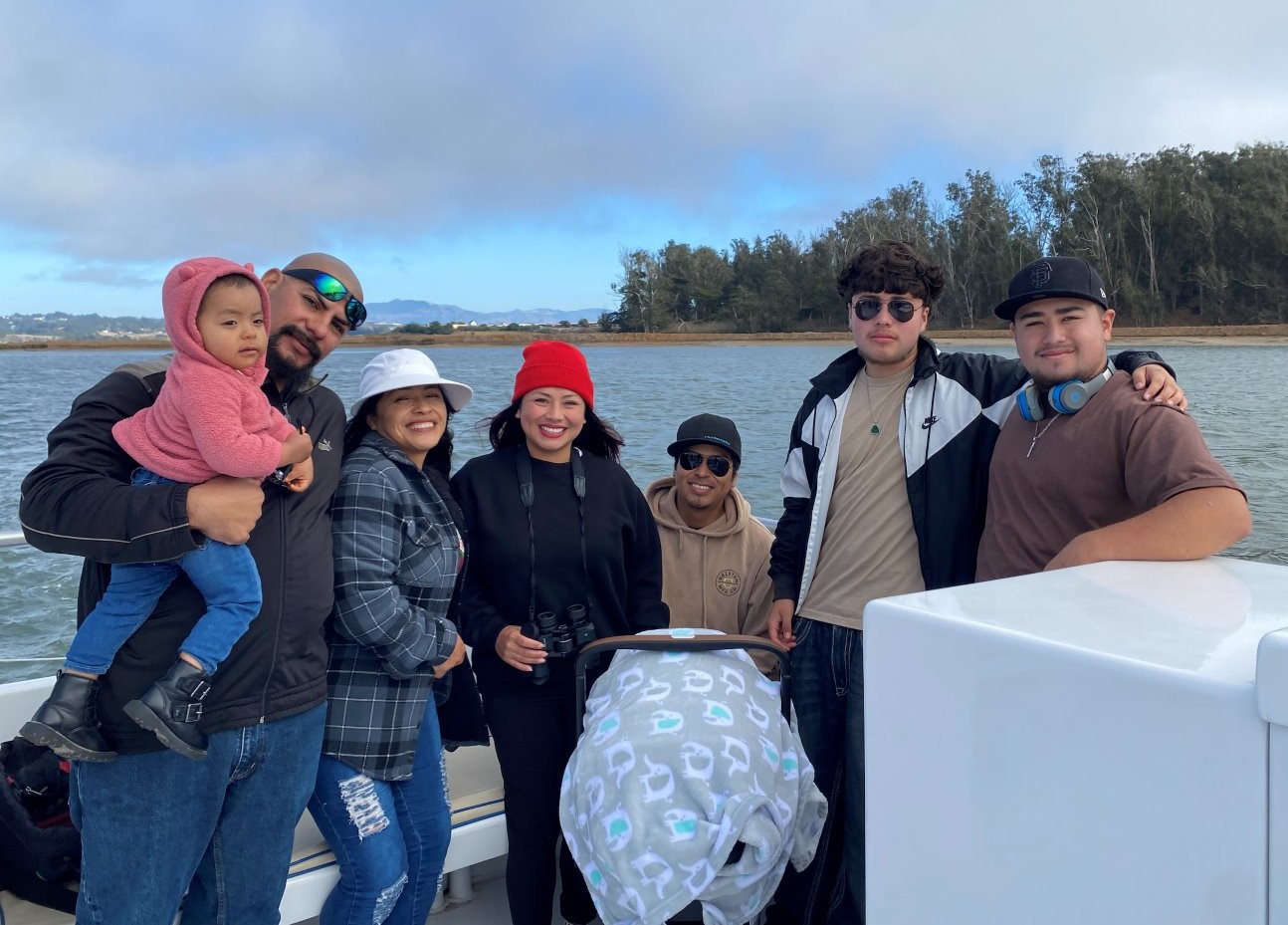 A family smiles for the camera as they stand on a boat with the shoreline in background.