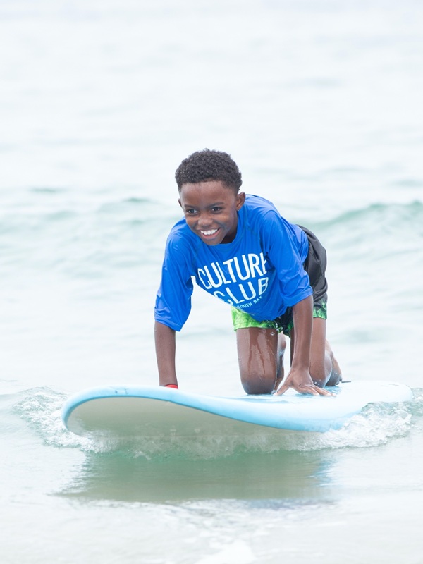 A youth crouches on a surfboard over coastal water sporting a smile.
