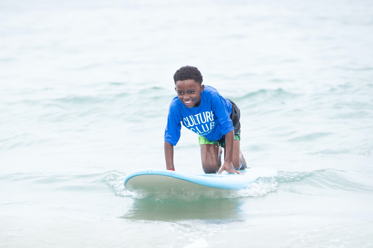 A youth crouches on a surfboard over coastal water sporting a smile.